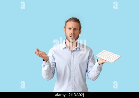 Confused man with keyboard on color background Stock Photo