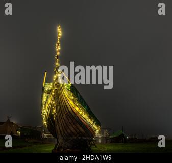 Viking ship with glowing Christmas lights at night on a lawn in the harbour of Roskilde, Denmark, January 1, 2022 Stock Photo