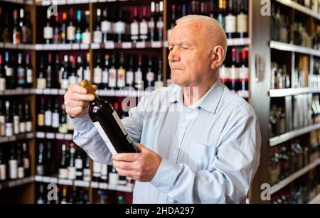 Elderly man chooses red wine in a liquor store Stock Photo