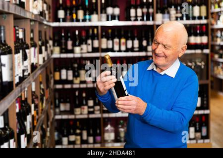 Elderly man chooses red wine in a liquor store Stock Photo