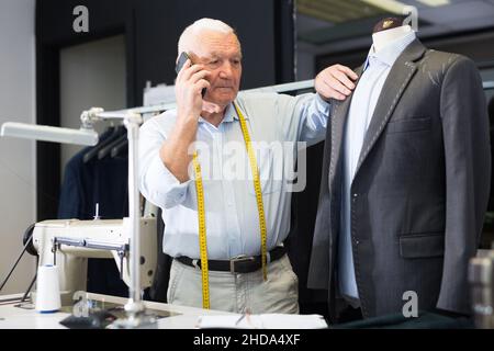 Professional tailor man talking on mobile phone and making notes in notebook Stock Photo