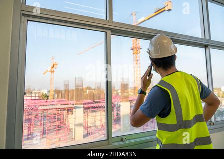 Architect or Engineer inspects the job site and works with a mobile phone, Crane on the construction site background. Stock Photo