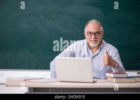 Old teacher in front of green board Stock Photo
