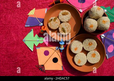 Til Gul or Sweet white sesame seeds Laddu with kites and phirki. Makar sankranti festival food background. Til baati with laddo Stock Photo