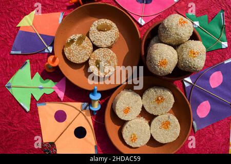 Til Gul or Sweet white sesame seeds Laddu with kites and phirki. Makar sankranti festival food background. Til baati with laddo Stock Photo