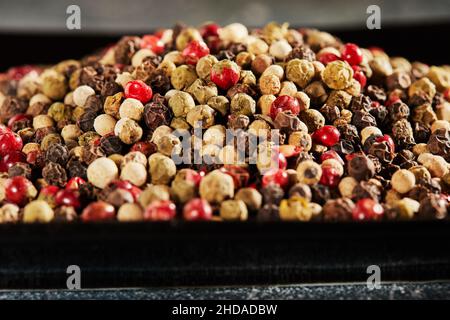 Multi-colored peppercorns on black plate with reflection Stock Photo