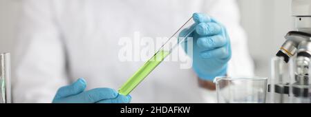 Scientist in protective gloves holds test tube with green liquid closeup Stock Photo