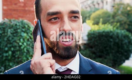 Portrait of entrepreneur man standing outside in front of startup office building talking at smartphone explaining company strategy to remote manager working at business presentation. Outdoors concept Stock Photo