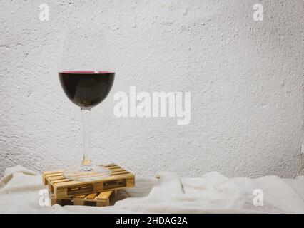 glass of red wine half full stands on mini pallete rest with blank space white retro background. Concept of transportation and delivery of wine. Stock Photo