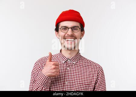 Very good. Satisfied young man approve new product, smiling and laughing pleased, give thumb-up like something really cool, standing white background Stock Photo