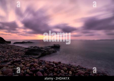 Sunrise on rocky beach in long exposure. Clouds outside, lonely beach, silk effect, orange colours. Stock Photo
