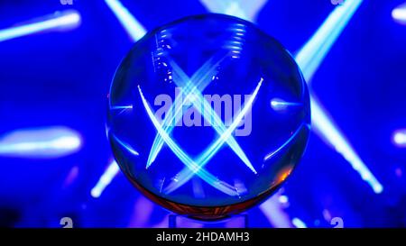 A crystal ball with colored reflections in the form of white and blue rays of light on a black background and blue and white rays. Stock Photo