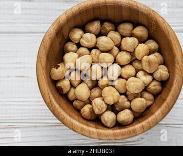 Peeled hazelnuts in a bowl on white wooden background Stock Photo