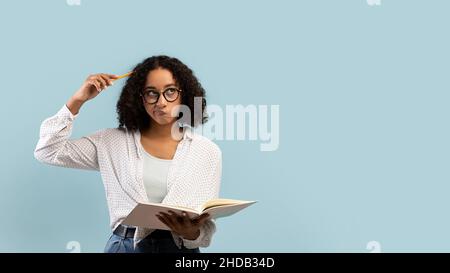 Thoughtful young black female student reading book, thinking over something on blue background, banner with copy space Stock Photo