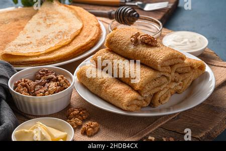 Homemade stuffed pancakes with sweet filling on a dark background with nuts, honey and sour cream. Pancake day. Side view, close-up. Stock Photo