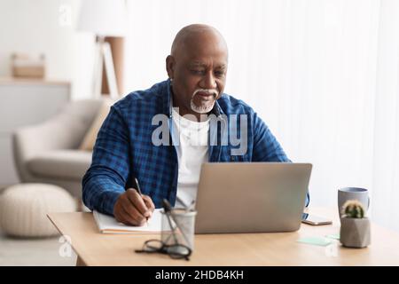 Senior Black Man Using Laptop Taking Notes Working At Home Stock Photo
