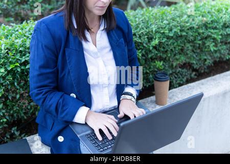 Unrecognizable beautiful Caucasian businesswoman using a laptop computer sitting outside an office building. Stock Photo