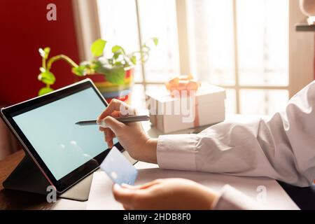 Woman using digital tablet with credit card, ordering online shopping christmas gifts. Working from home concept Stock Photo