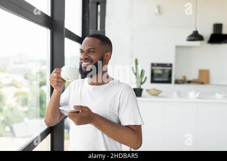 Smiling African American man drinking coffee looking through window Stock Photo