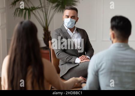 Young couple sitting at therapy session with therapist in facemask Stock Photo
