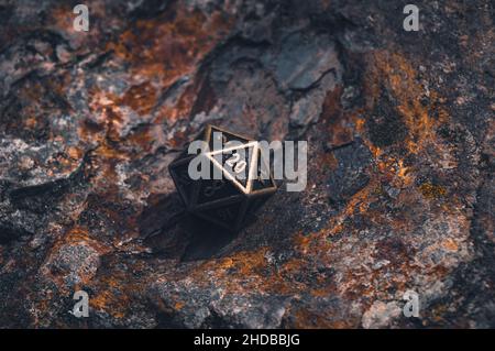 Metal D20 on a rocky surface with orange lichen in day light Stock Photo