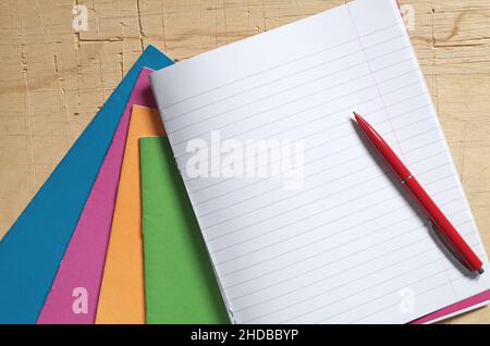 Colored school notebooks and red pen on old wooden desk, top view Stock Photo
