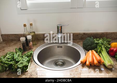 Various fresh raw healthy vegetables around sink on kitchen counter at home Stock Photo