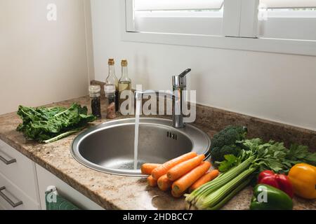 Various fresh raw healthy vegetables on kitchen counter while running water in sink at home Stock Photo