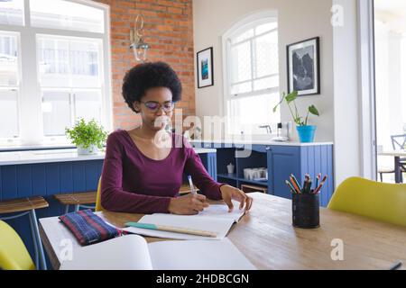 African american teenage girl writing in book while studying at home Stock Photo