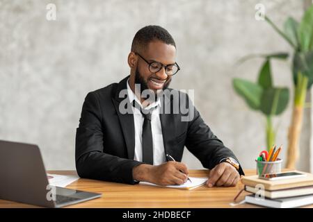 African American man using laptop writing in notebook Stock Photo