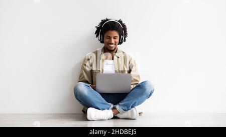 Happy Young African American Guy In Wireless Headphones Using Laptop Stock Photo