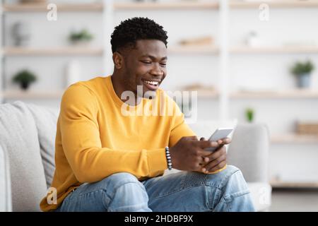 Handsome black guy chatting with girlfriend, using cellphone at home Stock Photo