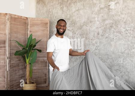 Smiling young African American man making bed in the morning Stock Photo
