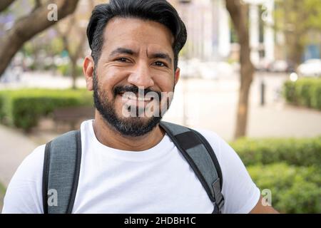 portrait of latin man with beard smiling at camera carrying a backpack Stock Photo