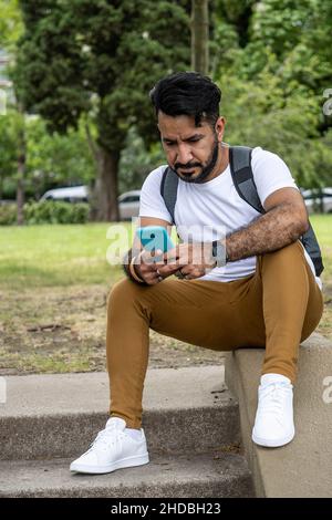 latino man sitting on the stairs of a park using his cell phone Stock Photo