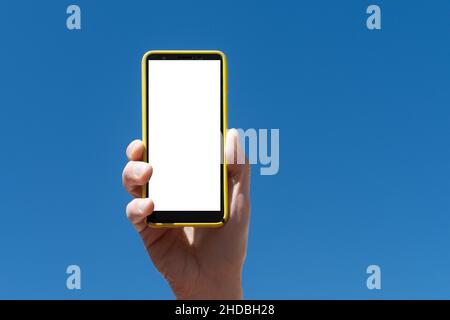 Hand holding a smartphone vertically, outdoors, with sky and greenery in the background, a sunny day Stock Photo