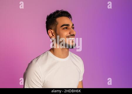 Handsome happy young Arab man in white t-shirt looking aside and smiling in neon light, copy space Stock Photo