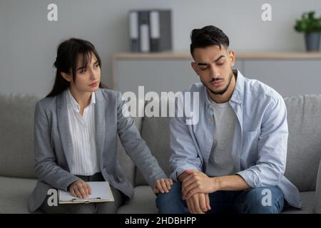 Loneliness, despair and depression concept. Professional psychologist comforting unhappy man, sitting in office Stock Photo