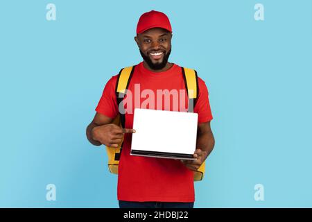 Food Delivery Website. Smiling black male courier holding laptop with blank screen Stock Photo