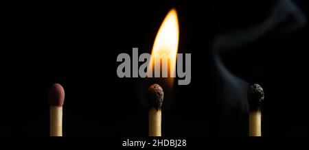 Closeup of three matches of an extinguished match next to a burning one on the black background Stock Photo