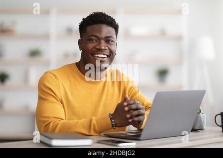 Portrait of positive black guy working on laptop Stock Photo