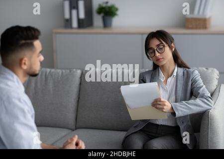 Psychotherapy concept. Focused female psychotherapist interviewing young man, listening and taking notes Stock Photo