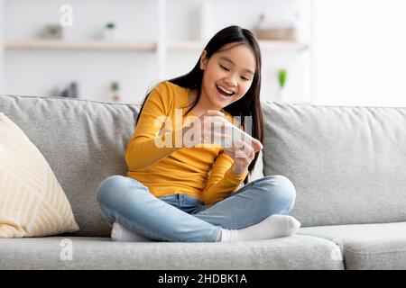 Emotional fmale kid having fun at home, using smartphone Stock Photo