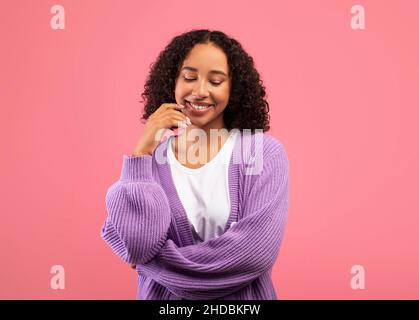 Thoughtful black woman touching chin and looking aside, considering interesting offer, standing over pink background Stock Photo