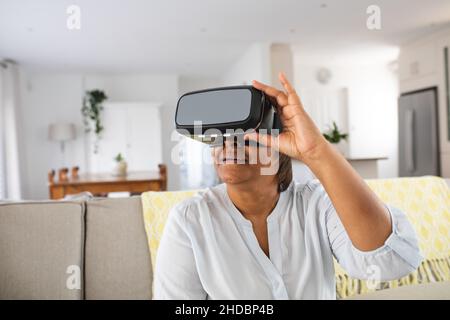 African american elderly woman using wearing virtual reality simulator at home Stock Photo