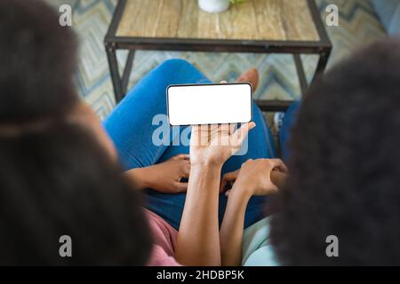 Mother and daughter using smart phone while sitting on sofa at home, copy space Stock Photo