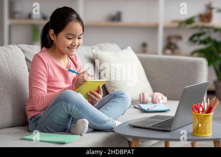 Smart asian kid studying at home, taking notes, using laptop Stock Photo