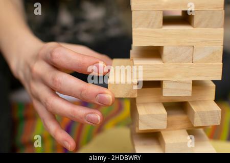 close up, the hand of a man, a girl, pulls a piece of wooden bar from the tower structure of a toy house during a board game Stock Photo