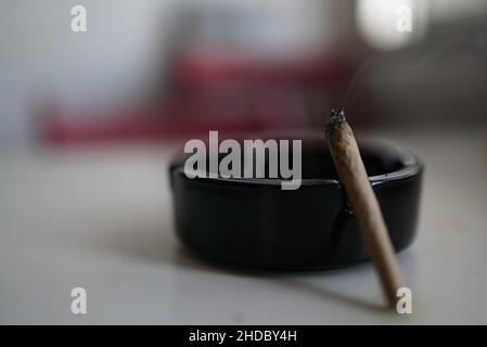 Close-up shot of ashtray with the cigarette on the table with blurred background Stock Photo