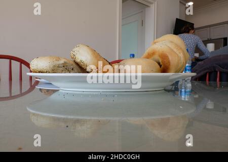 Side view of a white ceramic plate on a glass table top with assorted bagels; authentic home kitchen table with breakfast food item. Stock Photo